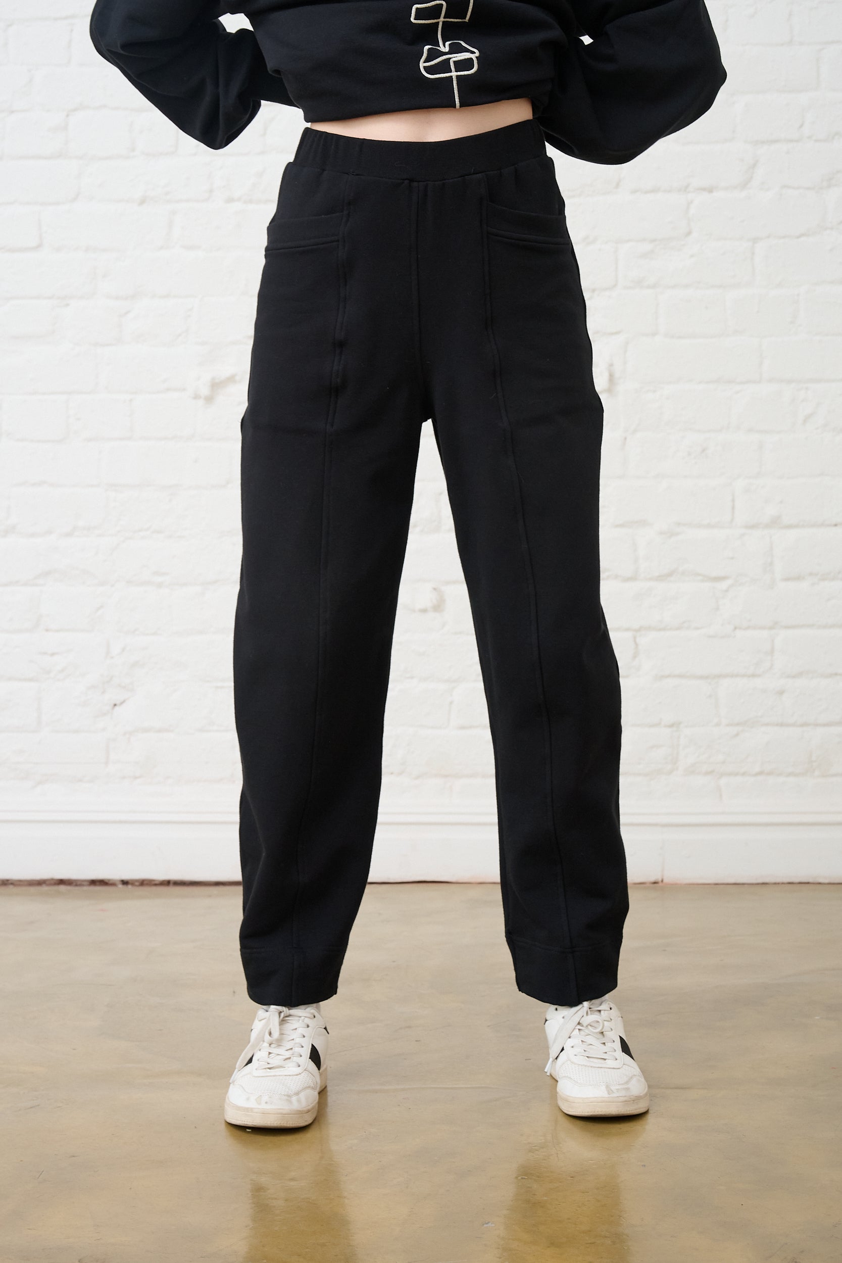 Model is wearing black barrel sweat pants with white sneakers and a matching top