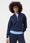 Model is wearing a navy quarter zip layered with a blue jumper and matching wide legs pants with leopard print sneakers  and brown accessories 