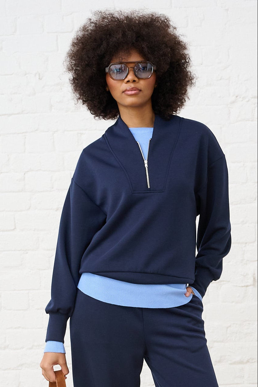 Model is wearing a navy quarter zip layered with a blue jumper and matching wide legs pants with leopard print sneakers  and brown accessories 