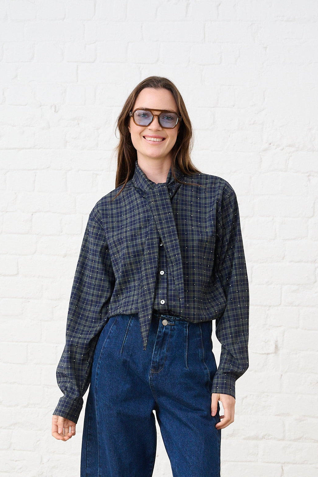 Model is wearing a check shirt with a bow tie detail and dark wash denim jeans 