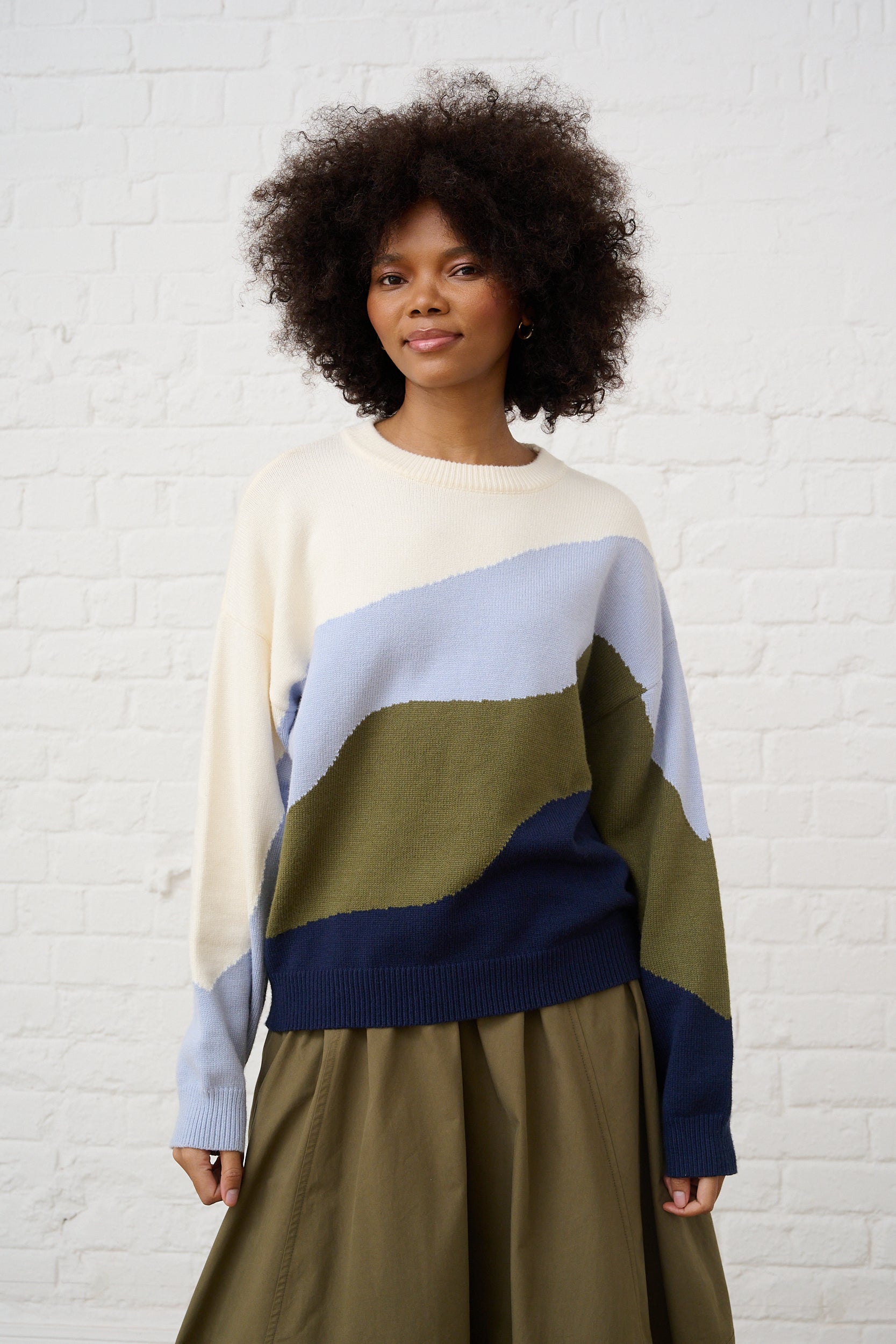 Model is wearing a knit sweater in blue and green marble wave with a green skirt 