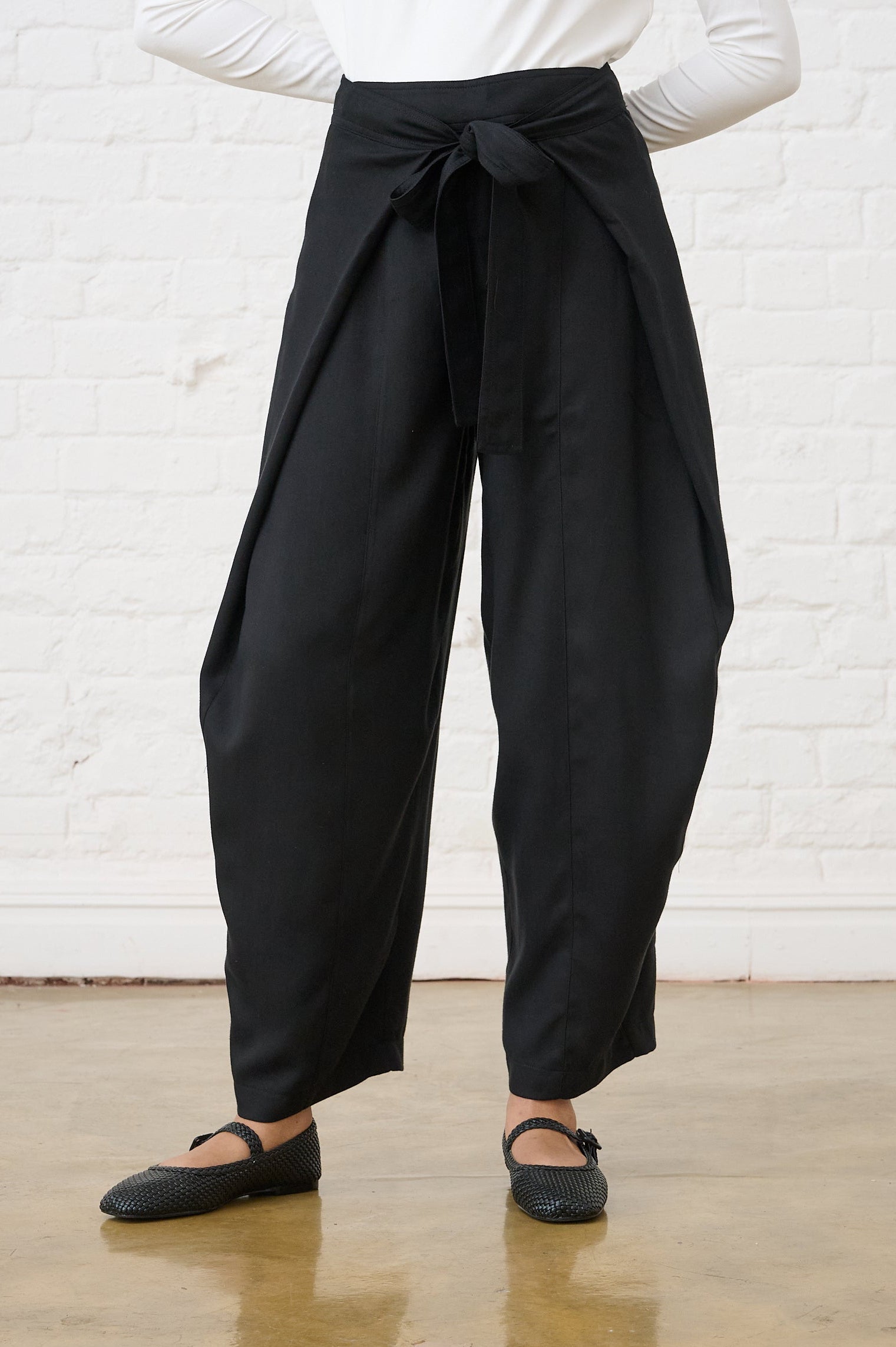 Model is wearing black pants with a front tie closure detail and black Mary janes, with a milk polo 