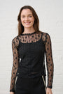 Model is wearing a black floral lace long sleeve top with black lace trim pants and a black cami underneath