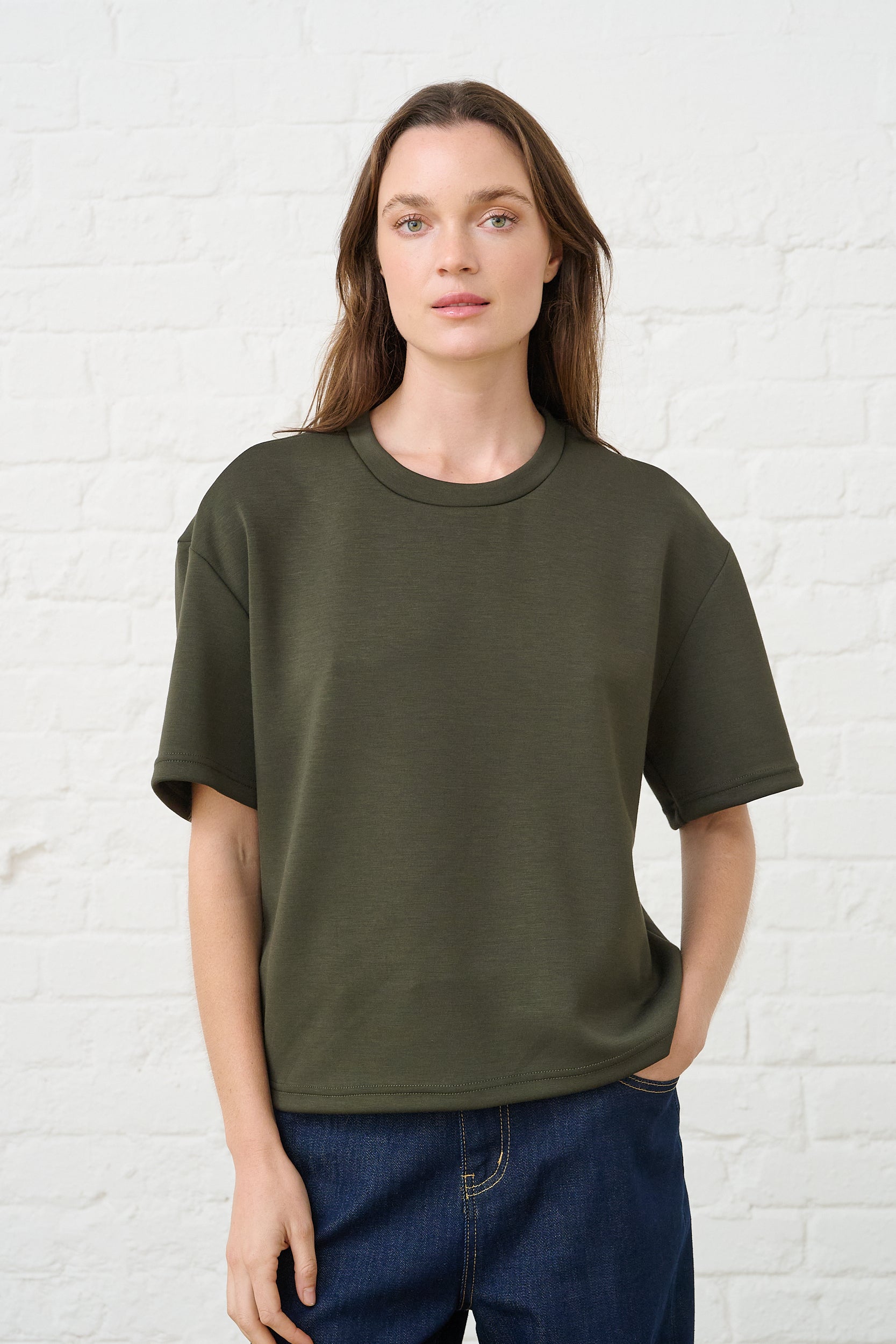 Model is wearing an olive green t shirt with dark wash denim jeans 
