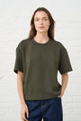 Model is wearing an olive green t shirt with dark wash denim jeans 
