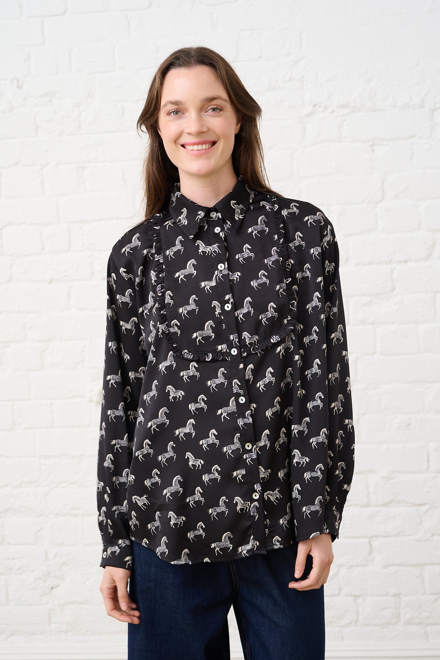 Model is wearing a black shirt with a pie crust bib in a horse novelty print, and dark wash denim jeans 
