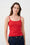 Woman wearing a red tank top and blue jeans against a white brick wall.