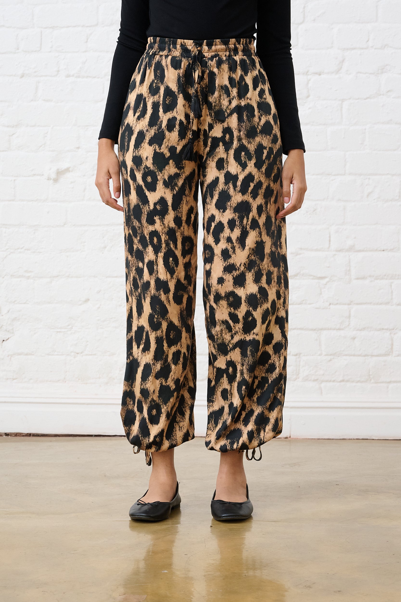 Model is wearing animal print haram style pants with a black top and lack pumps