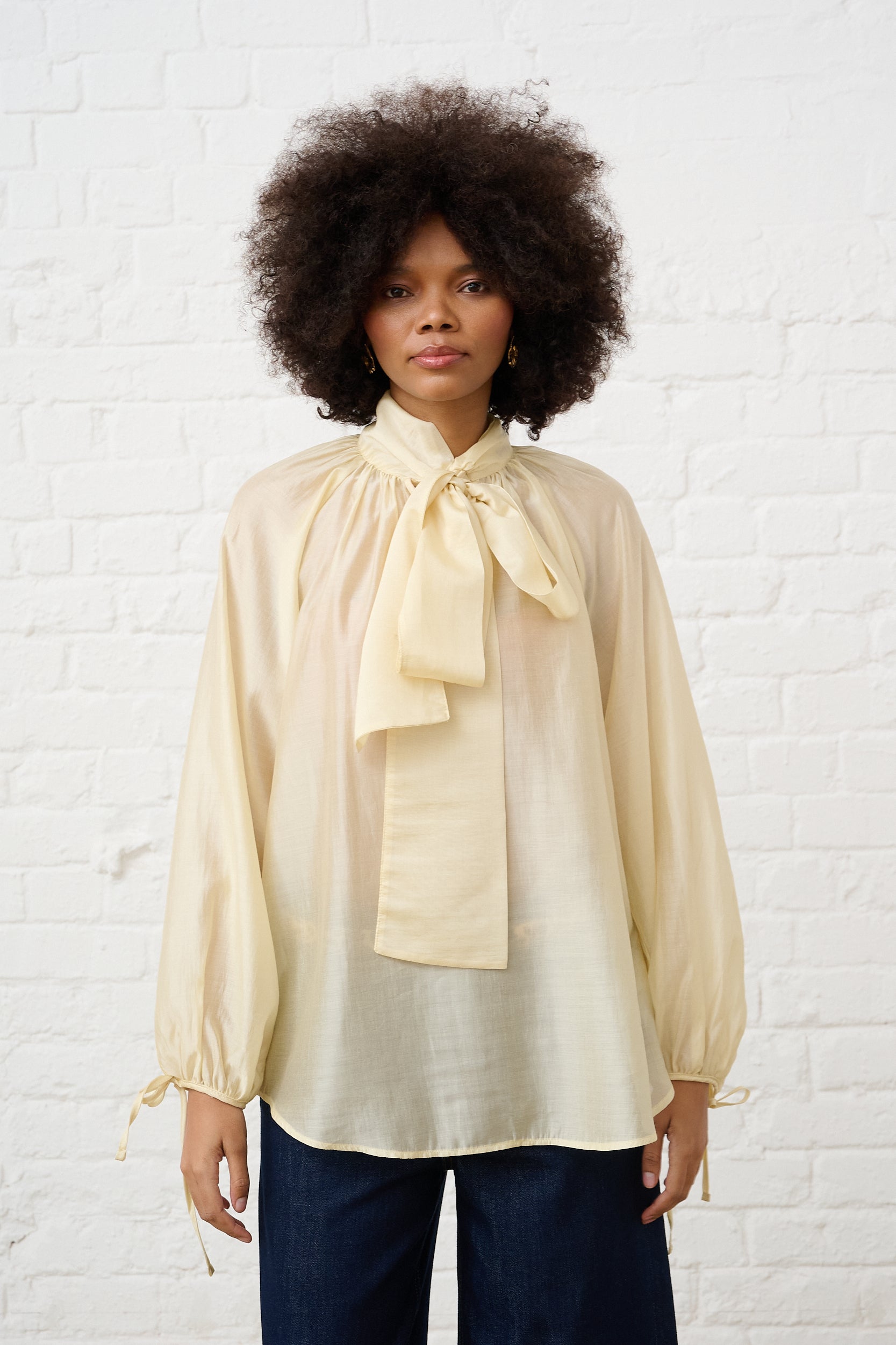 Model is wearing a butter yellow blouse with a tie detail and blue denim jeans