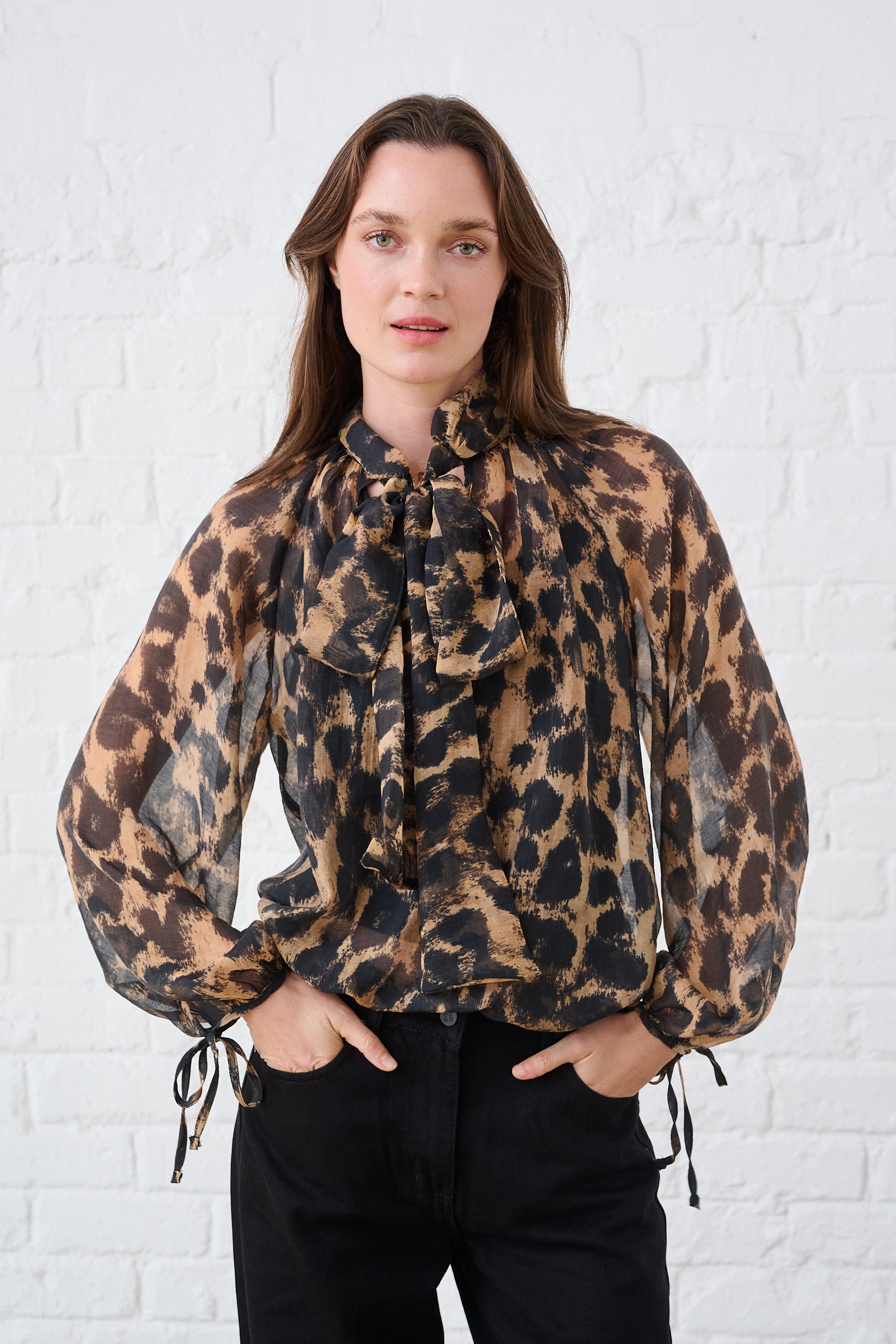 Model is wearing a women's animal print blouse with tie-neck detail, gathered neckline, full sleeves with tie cuffs and a lightweight sheer finish.