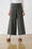 Model is wearing wide leg olive bengaline pants with contrast stitching and brown shoes 