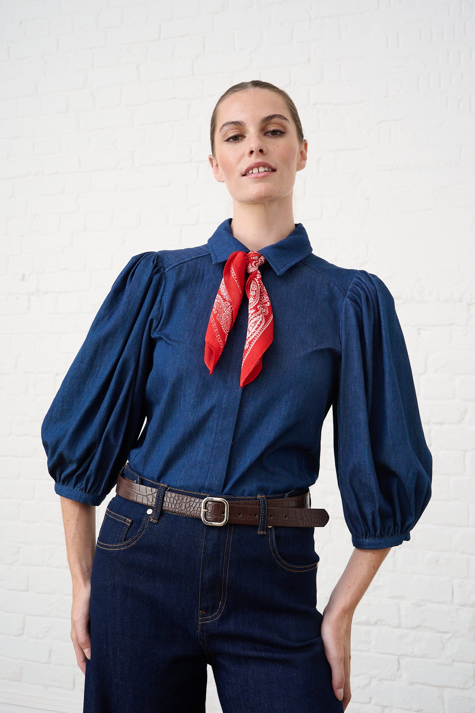 Model is wearing a denim puff sleeve blouse and a red bandana scarf with denim jeans and a brown belt 
