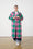 Model is wearing a long coat with green and pink check and dark wash denim jeans