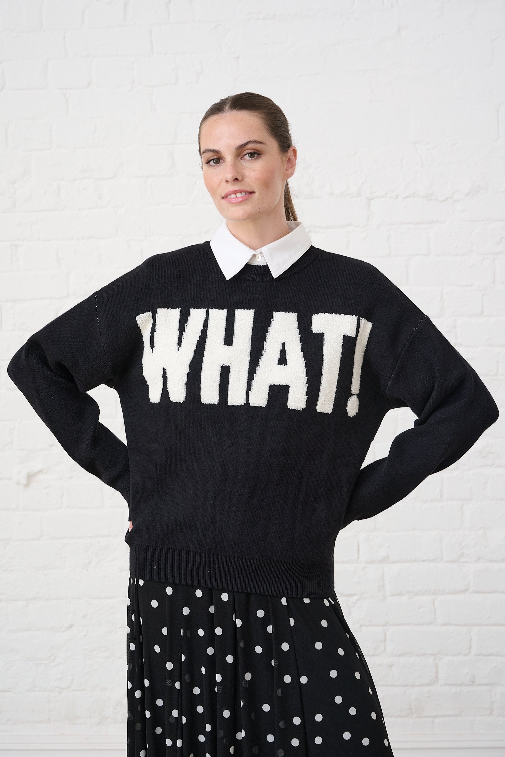 Model is wearing a black and white WHAT! knit sweater with a polka dot skirt and white shirt