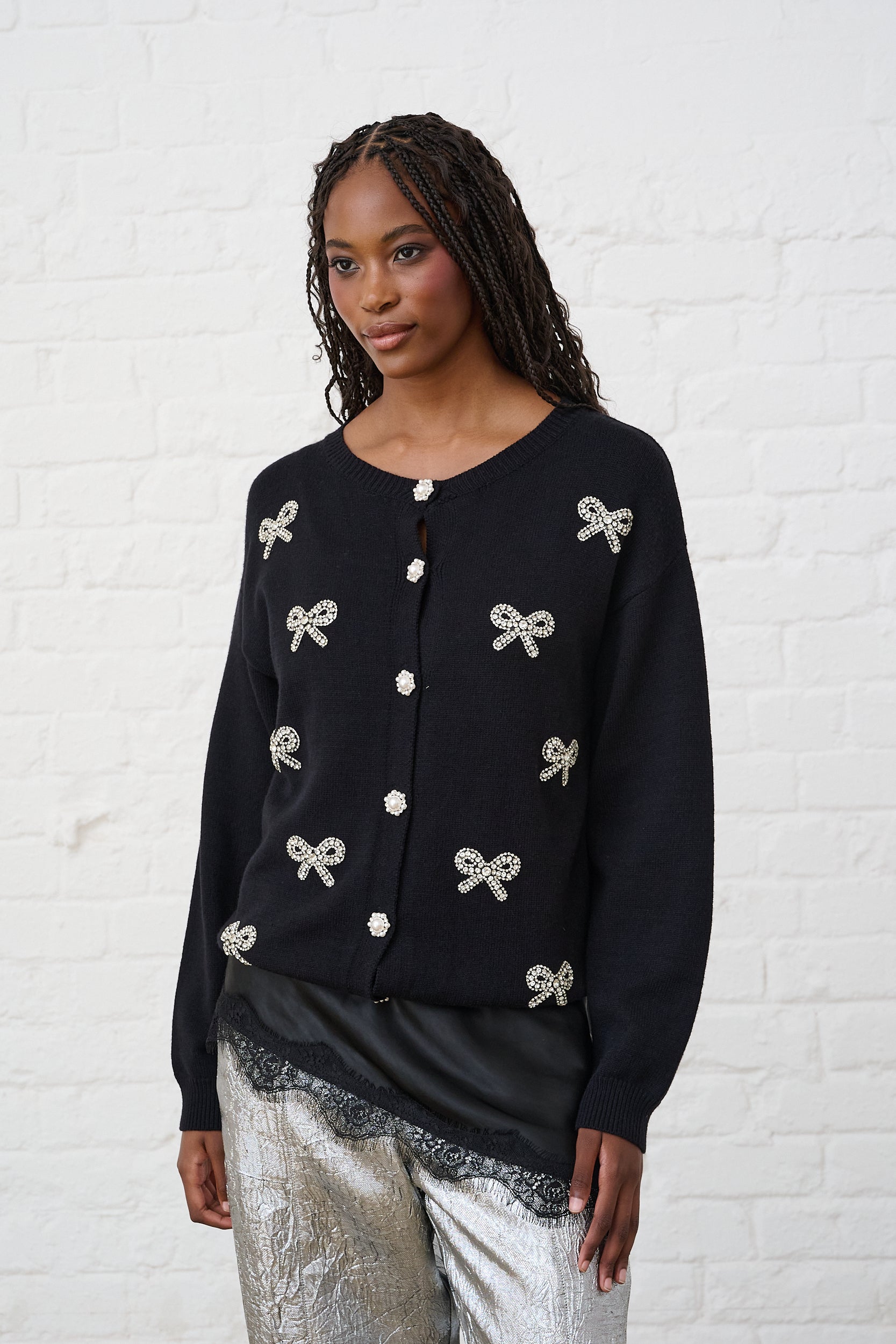 Model is wearing a black cardigan with silver bow embellishments and silver pants with a lace cami