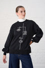 Model is wearing a black sweat shirt with white line art detail , with denim jeans and a white polo neck