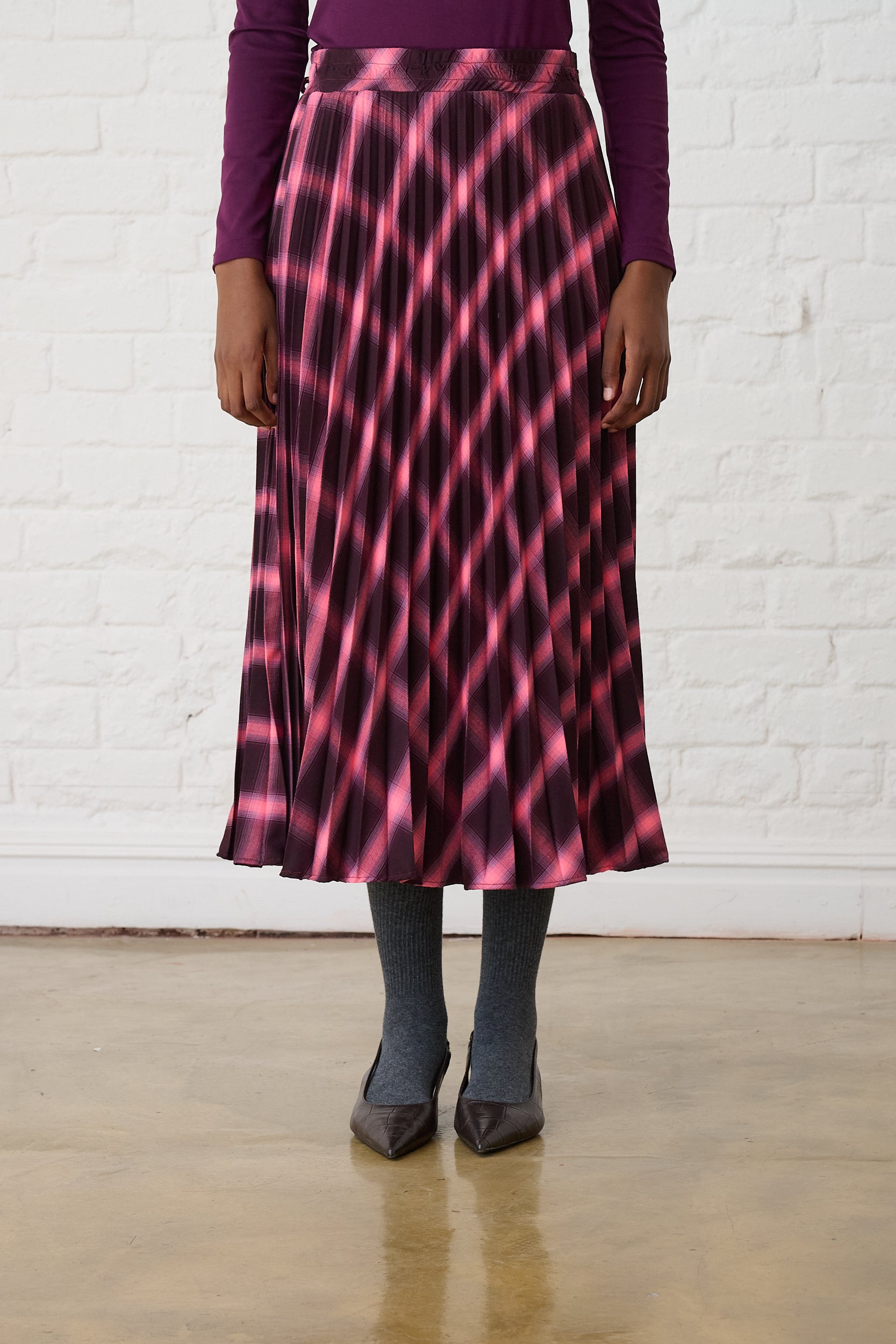 Model is wearing a burgundy check pleated maxi skirt with burgundy shoes and top