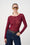 Model is wearing a burgundy long sleeve mesh top with dark wash denim jeans and a brown belt 