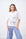 Woman wearing a white t-shirt with floral embroidery and blue checkered pants against a white brick wall.