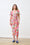 Woman wearing a colorful floral dress standing against a white brick wall.
