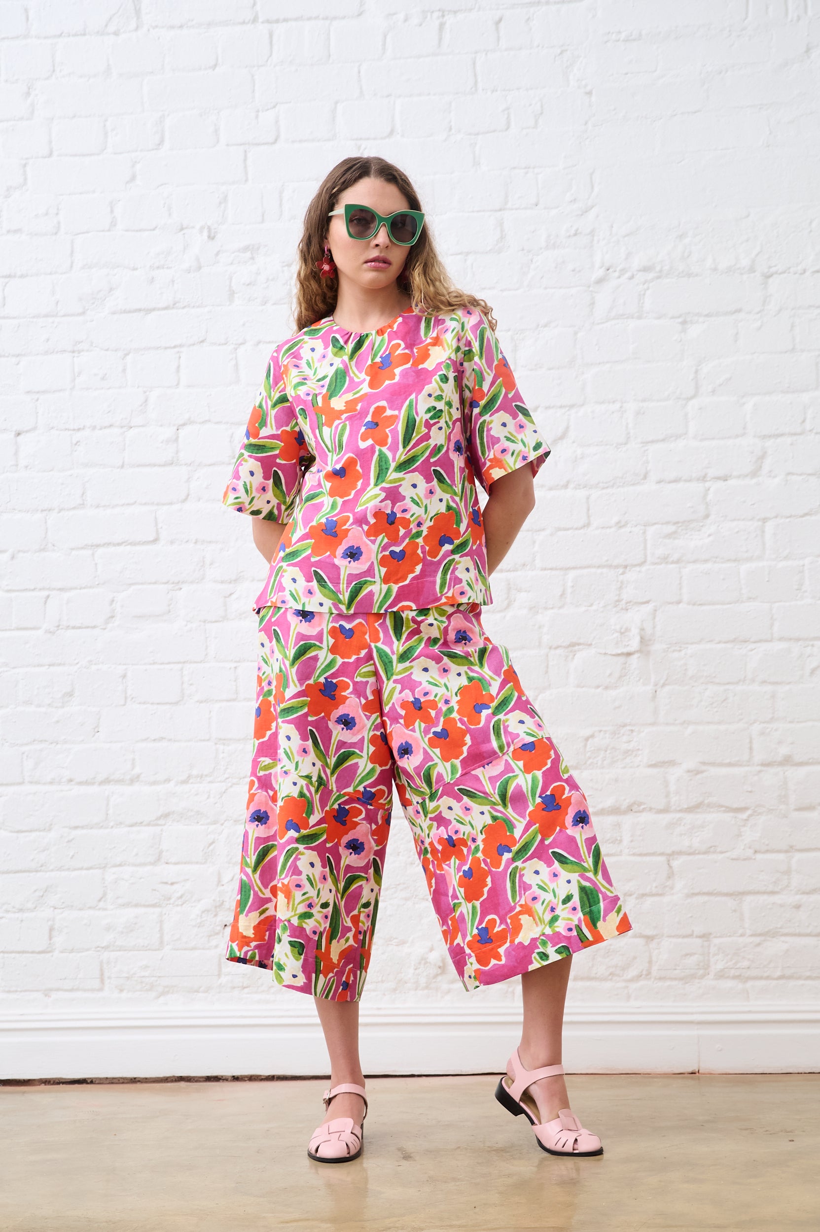 Woman wearing a colorful floral outfit against a white brick wall.