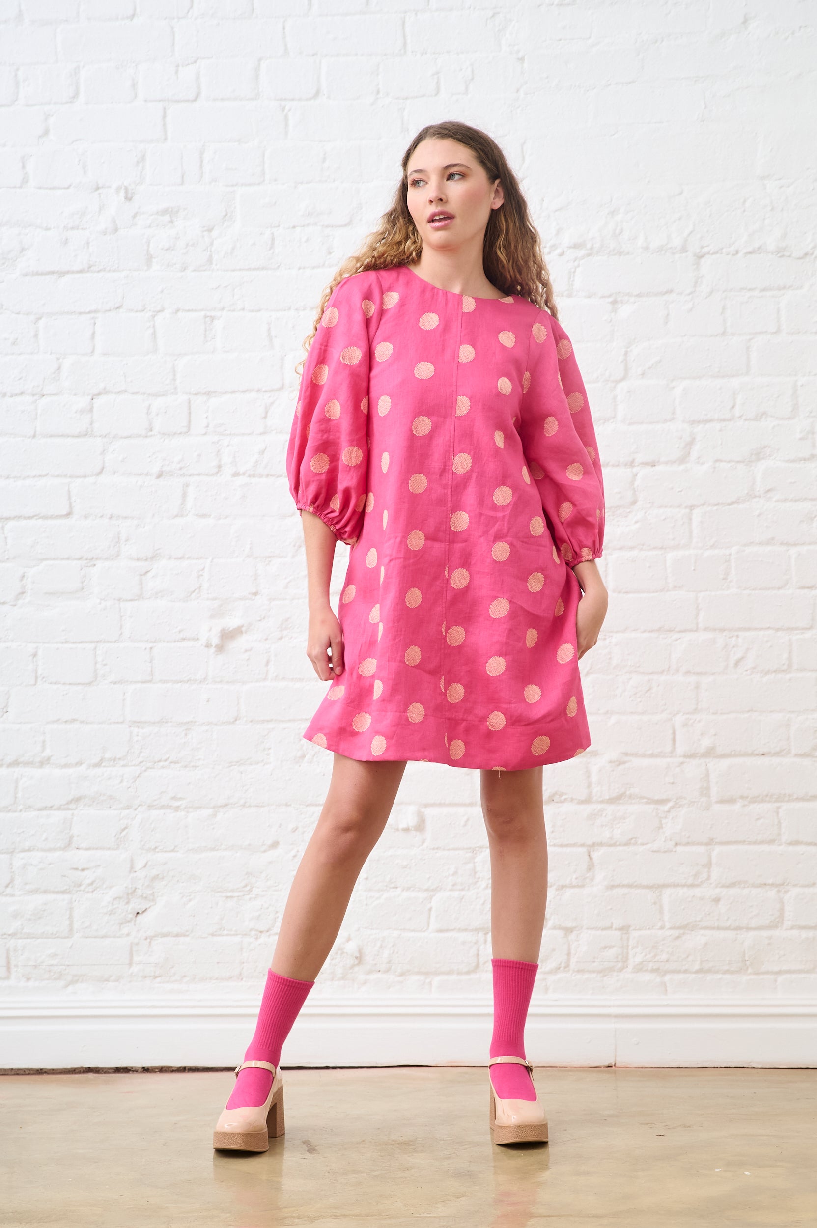 Model is wearing a pink and gold spot midi dress with pink socks and pin shoes