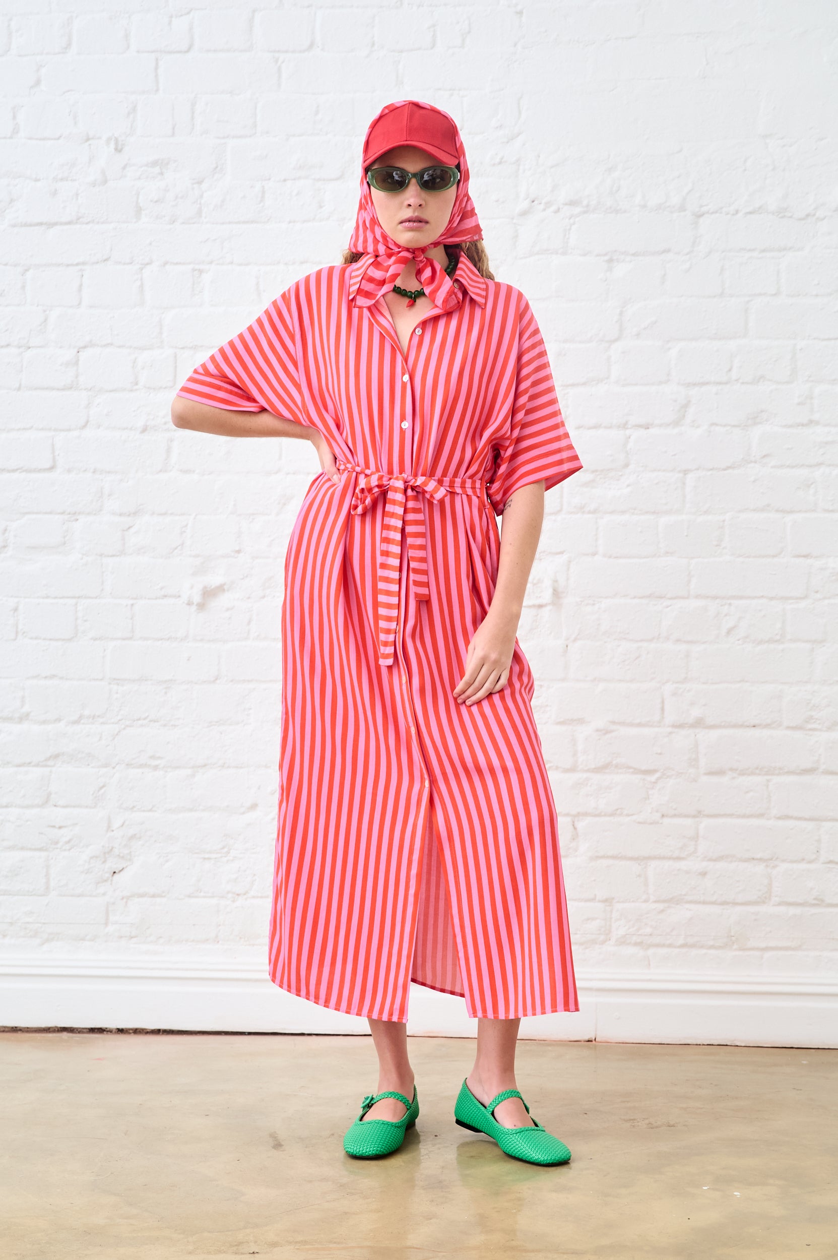 Person wearing a red and white striped dress with a matching headscarf against a white brick wall.