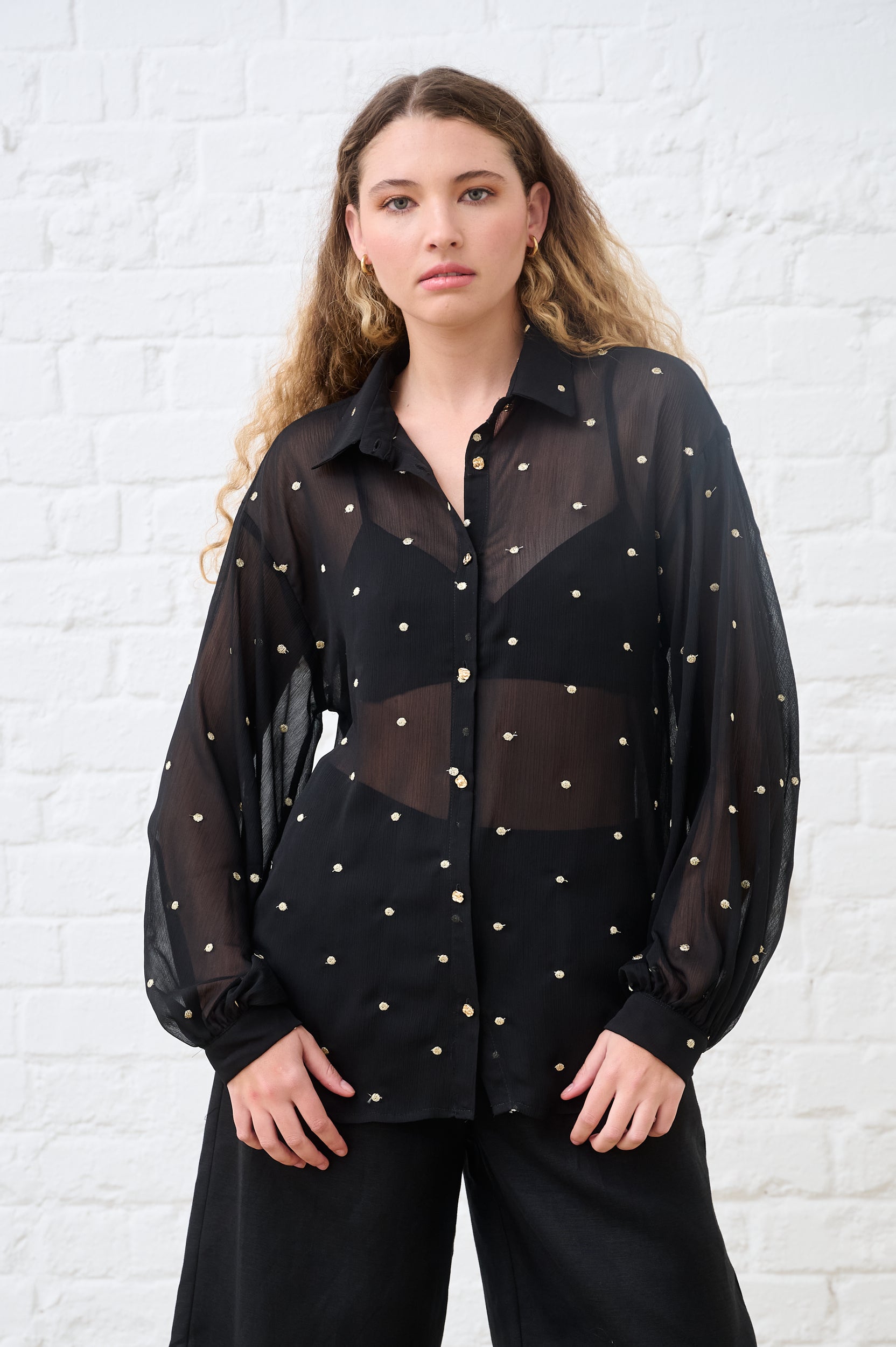 Model is wearing a black and gold sheer bellow sleeve short with black pants 
