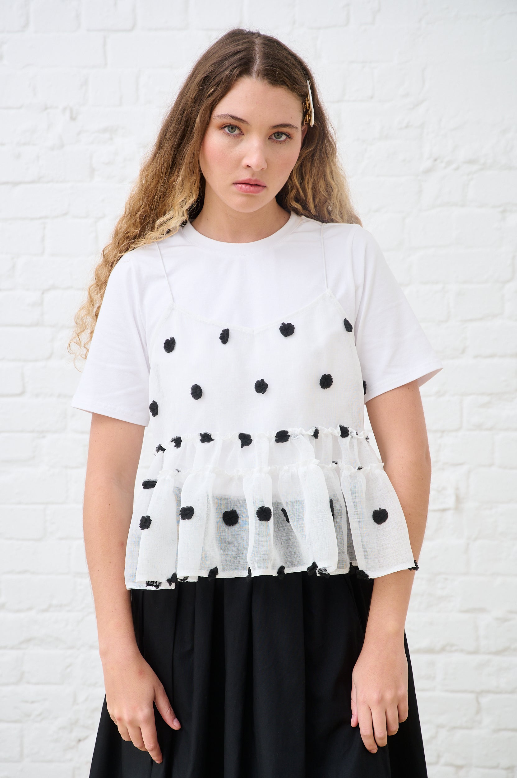 Model is wearing a black and white spot top with a black skirt