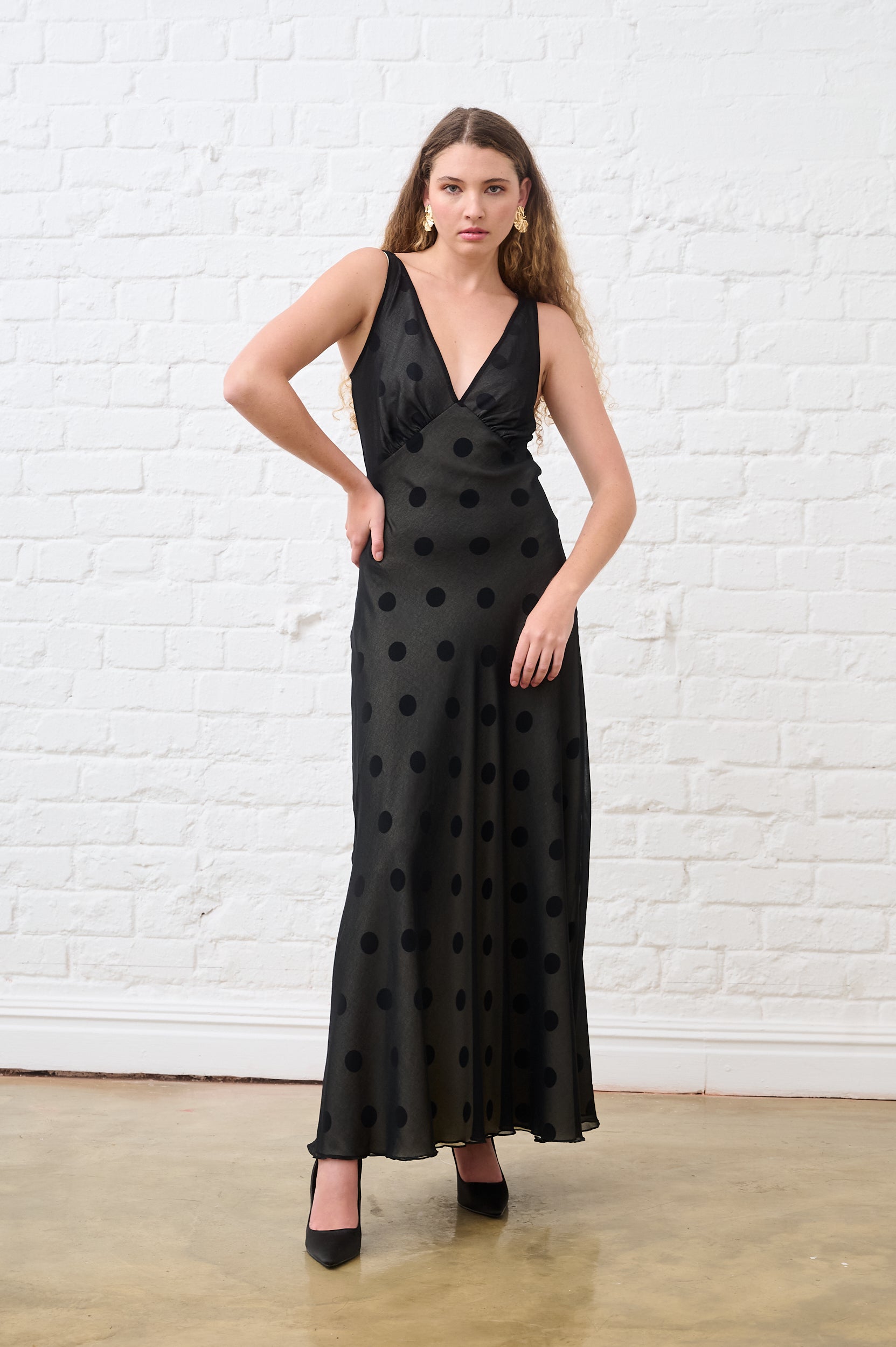 Model is wearing a sheer spotted black dress with black heels 