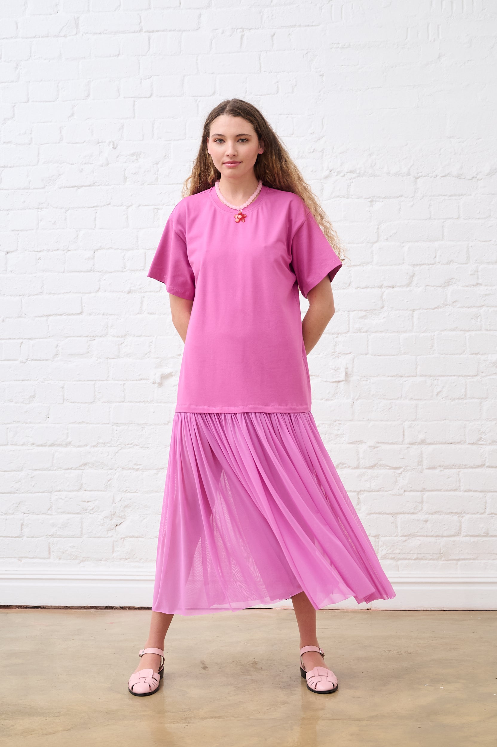 Woman wearing a pink dress against a white brick wall.