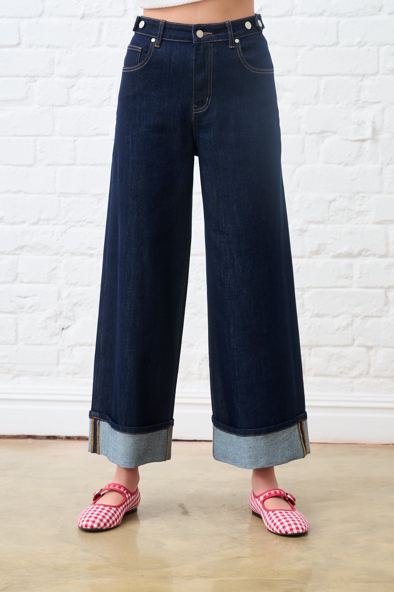 Person wearing dark blue wide-leg jeans with a white brick wall background