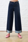 Person wearing dark blue wide-leg jeans with a white brick wall background