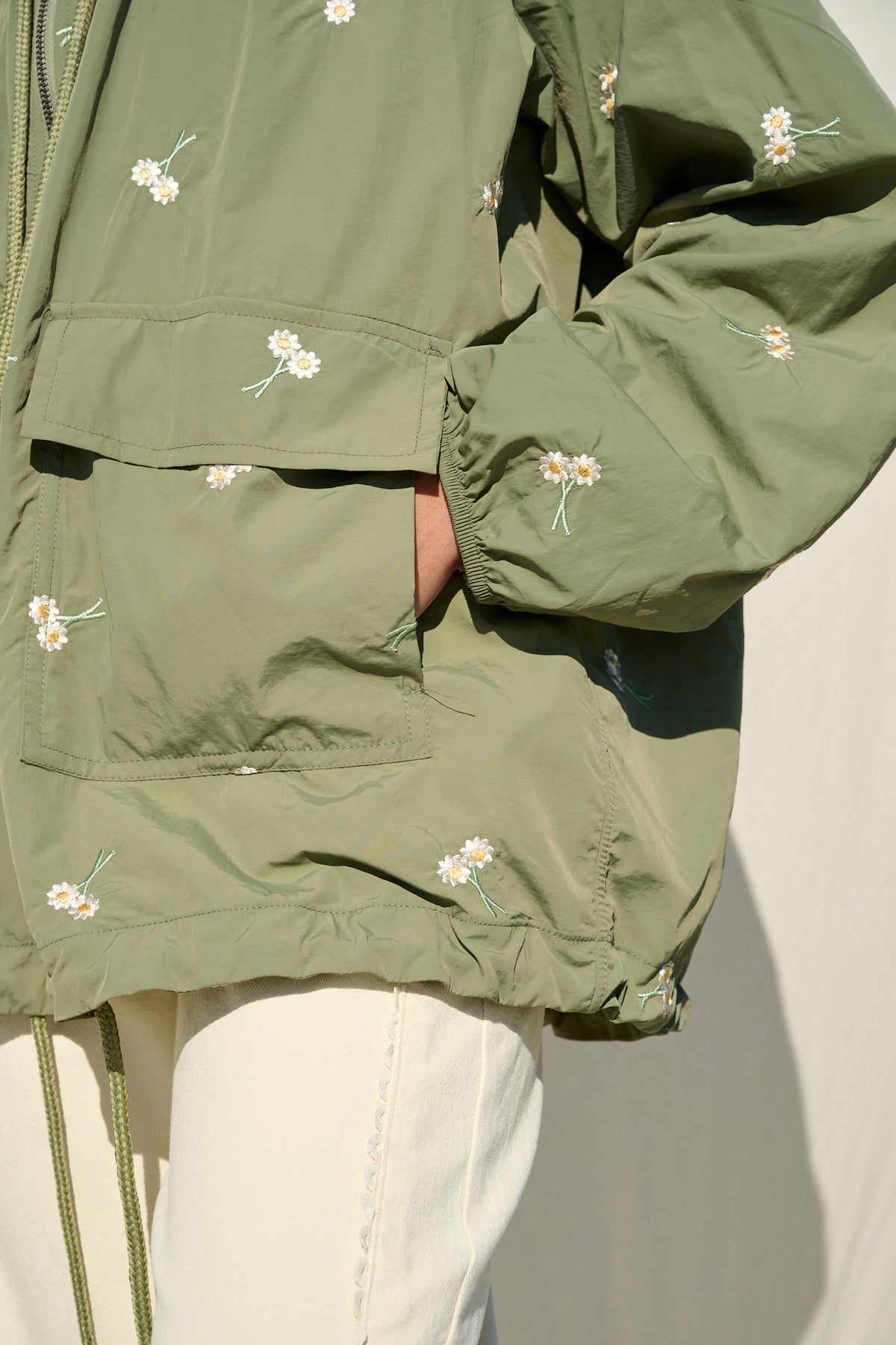 Model wearing fatigue green hooded jacket with daisy embroidery