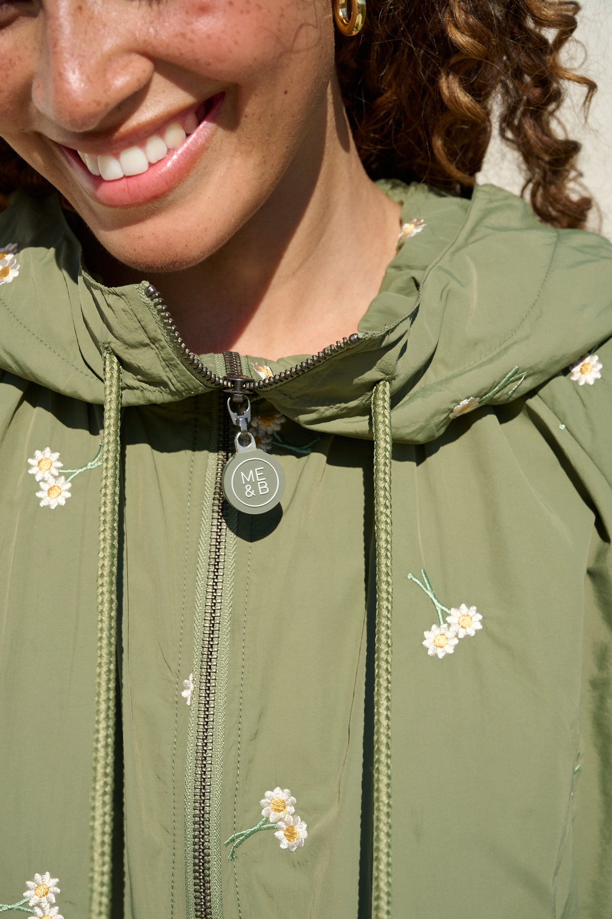 Model wearing fatigue green hooded jacket with daisy embroidery
