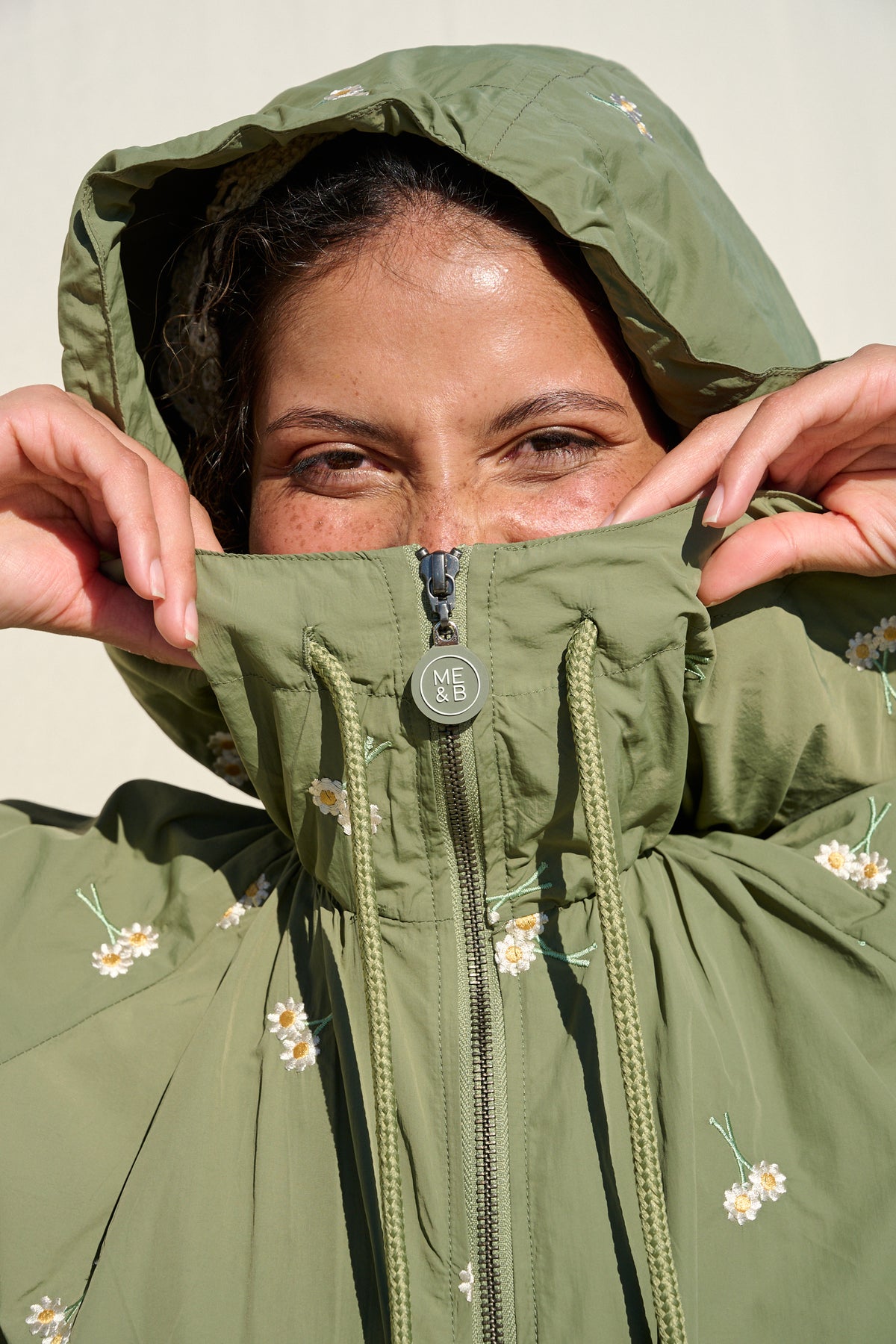 Model wearing fatigue green hooded jacket with daisy embroidery
