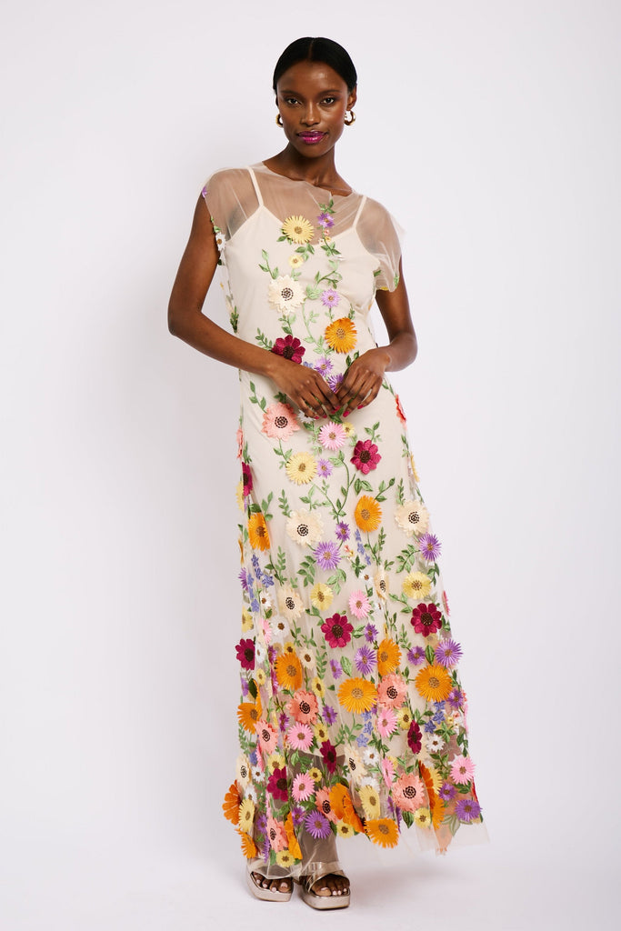 Model is wearing a maxi length mesh dress with capped sleeves and colourful floral applique applied all over