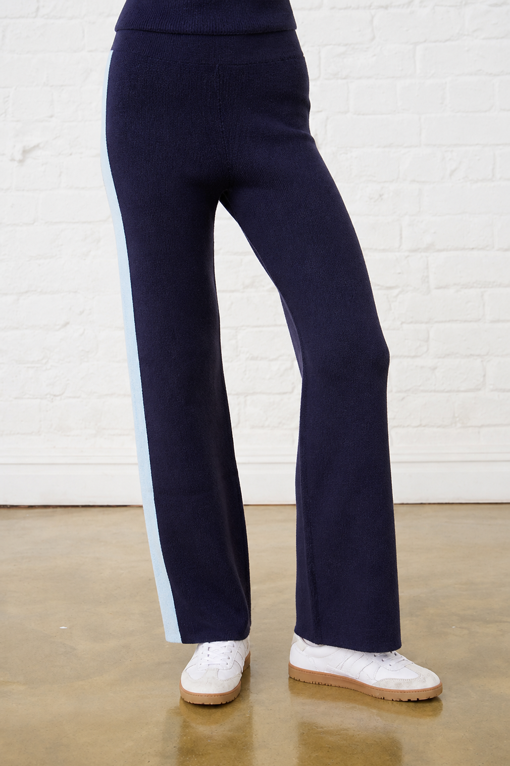 Navy pants with a light blue stripe worn by a person against a white brick wall.